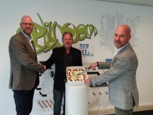 EMC-specialist HF Technology maakt sinds 1 november deel uit van de Elincom Group. Danny Langbroek (Elincom) en Sem Gorter (HF Technology) schudden elkaar de hand, terwijl Hans Zijlstra de taart aansnijdt.'